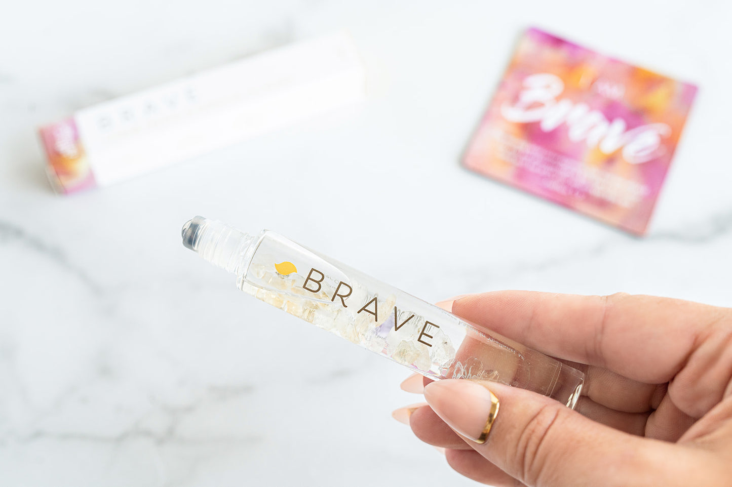 Hand holding a 'BRAVE' bottle with a colorful card in the background