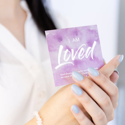 Hand holding a card with 'I AM Loved' text against a blurred background