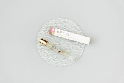 A Brave Crystal Essential Oil Roller Bottle Blend on a clear glass plate with the roller box sitting next to it 