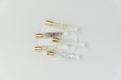5 crystal essential oil blend roller bottles on clear glass plate named Loved, Beautiful, Healing, Brave and Calm