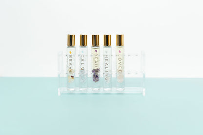 An acrylic clear roller bottle holder on a pale aqua and white background holding 5 crystal roller bottles with essential oil natural perfume blends