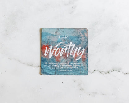 A Blue and red magnet that says I Am Worthy with a bible verse from Colossians 1:22 on a white marble background that says He has brought you into his own presence and you are holy and blameless