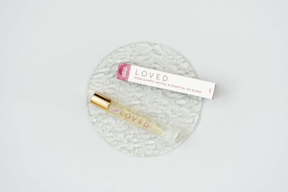 Loved Crystal Essential Oil Roller bottle blend on a clear glass plate with the box