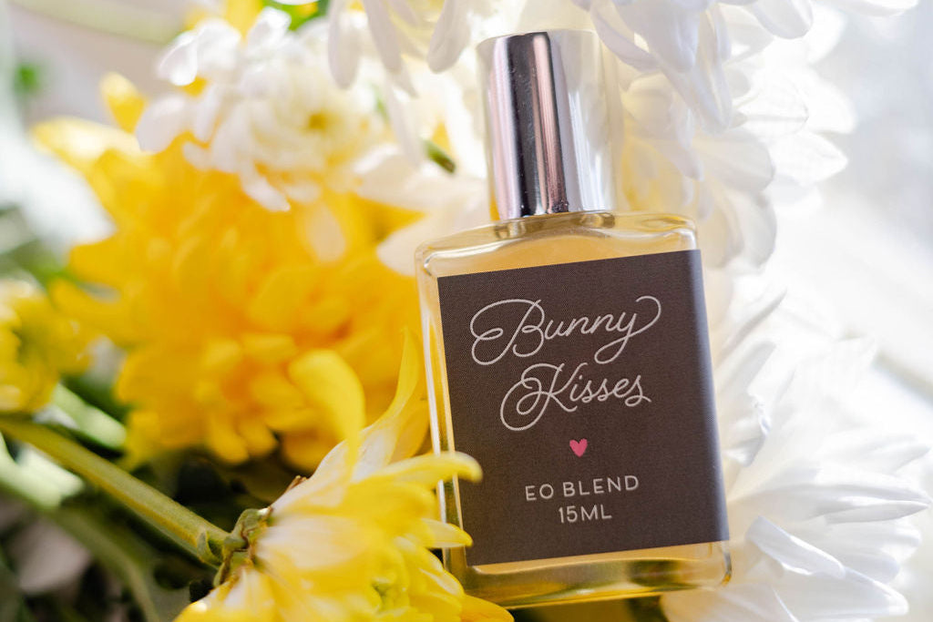 Perfume bottle labeled 'Bunny Kisses' surrounded by yellow and white flowers on a light background