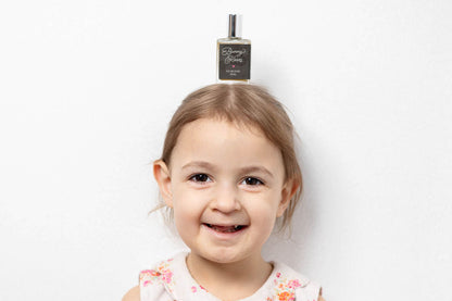 Young girl in a floral dress standing and smiling against a white background with a Bunny Kisses roller bottle on her head