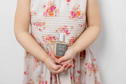 Little girl holding a bottle of perfume Bunny Kisses roller with a floral dress
