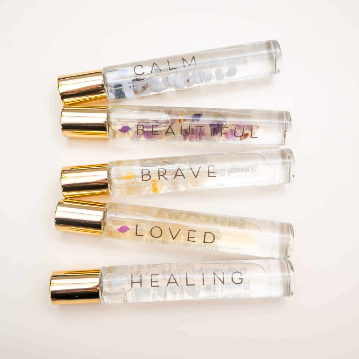 A collection of five clear roller blends with gold-colored caps, each labeled with different words such as 'CALM', 'BRAVE', 'LOVED', 'HEALING', and 'BEAUTIFUL'.