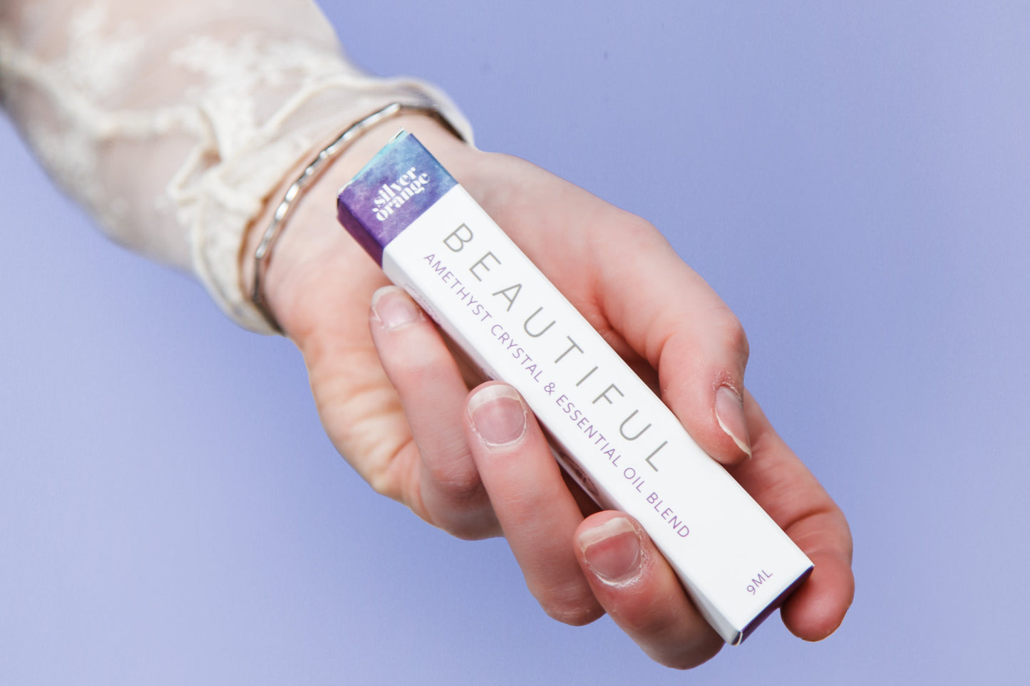 Hand holding a boxed roller with a visible brand name called Beautiful against a light purple background