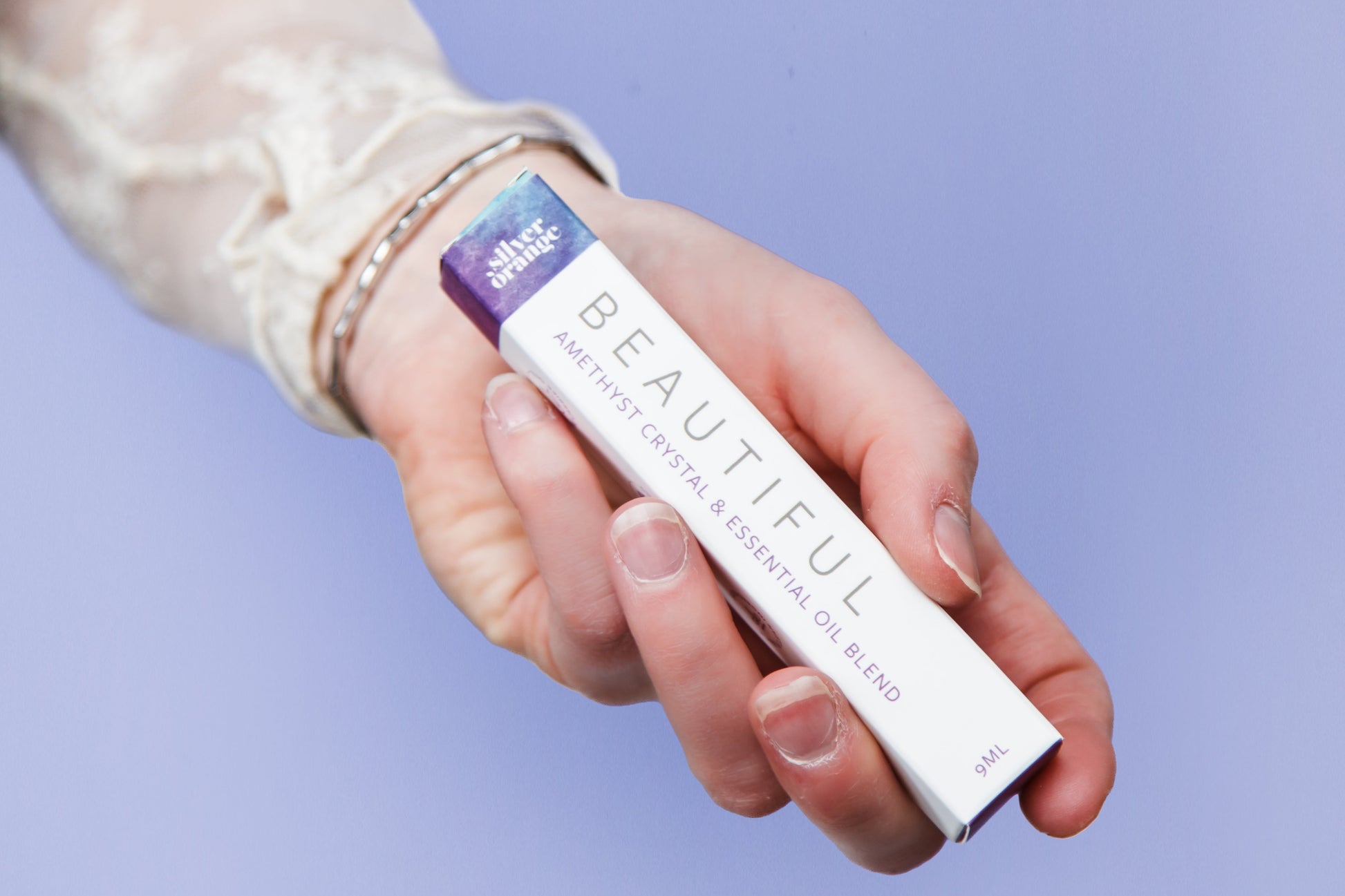 Hand holding a boxed roller with a visible brand name called Beautiful against a light purple background