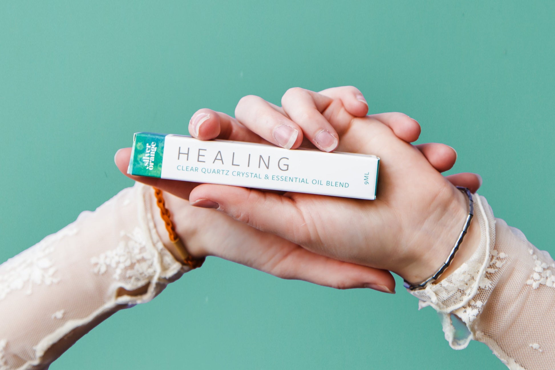 Two hands holding a tube labeled 'Healing' against a teal background
