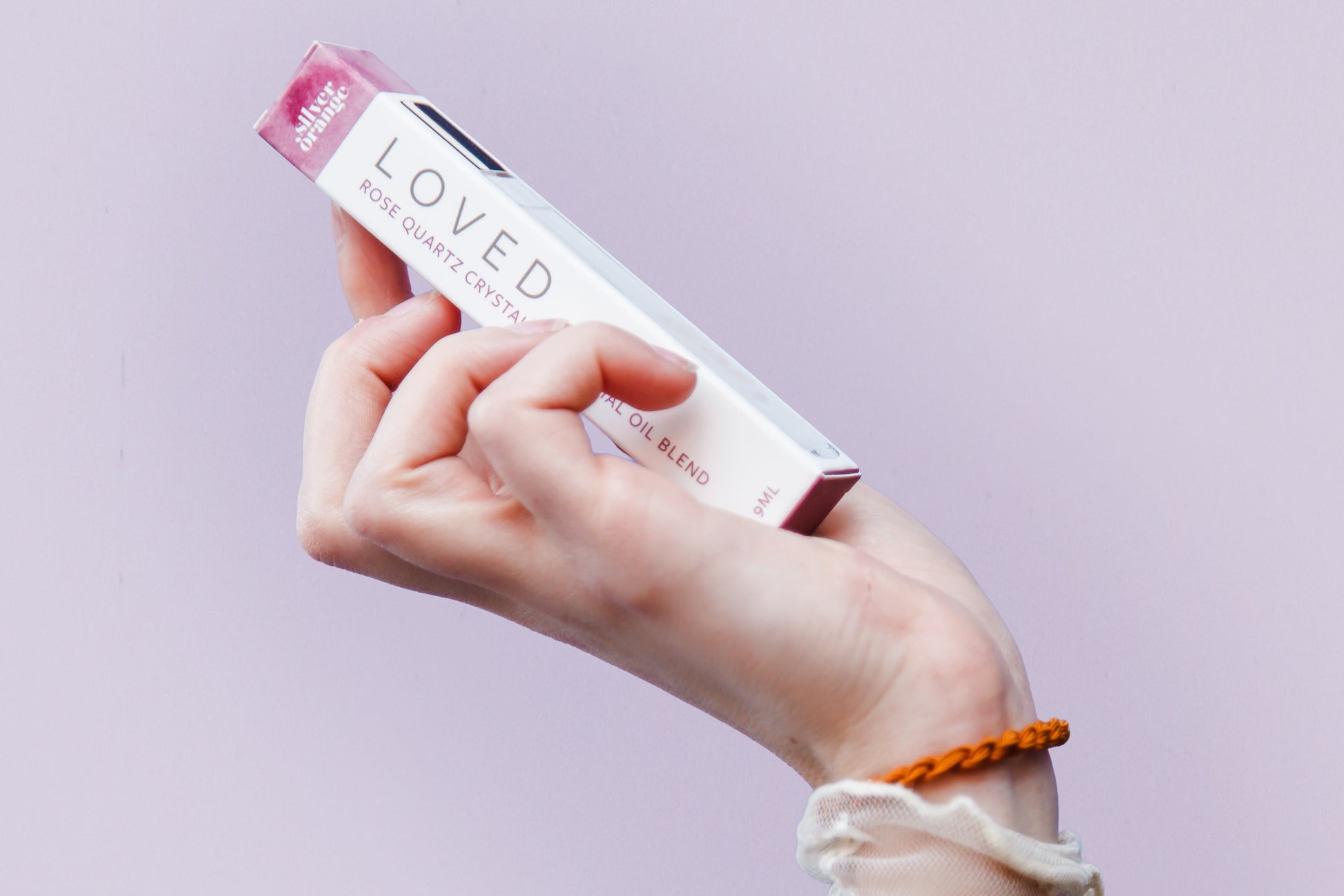 Hand holding a white and pink product labeled 'LOVED' against a light purple background
