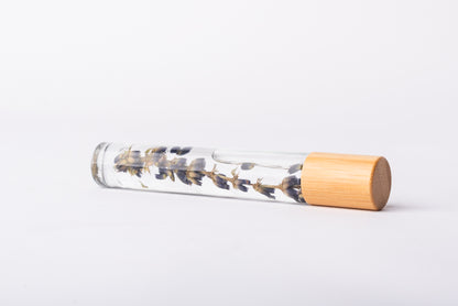 A clear glass roller bottle with Bamboo lid laying on it's side filled with an organic lavender sprig